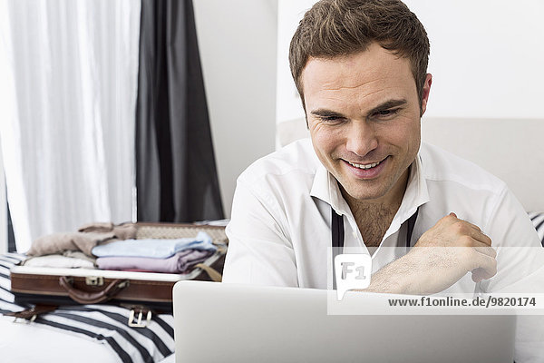 Businessman sitting on bed using laptop