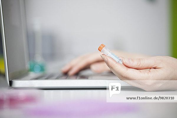 Nahaufnahme eines Wissenschaftlers mit Testprobe am Laptop