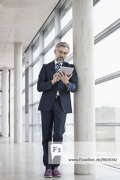 Geschäftsmann der sich mit Hilfe eines digitalen Tabletts gegen die Säule lehnt