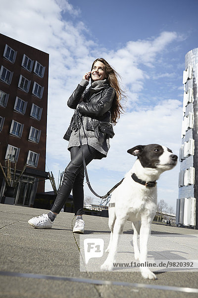 Germany  Dusseldorf  Young woman with dog using smart phone