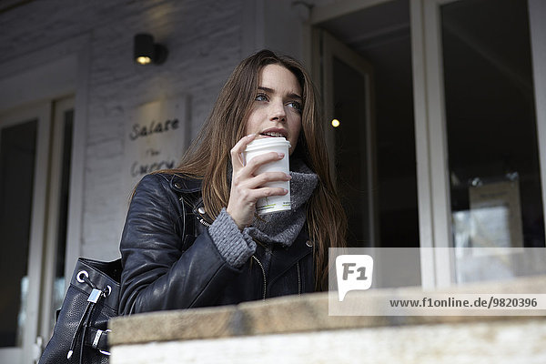 Germany  Dusseldorf  Young woman with coffee sitting outdoor