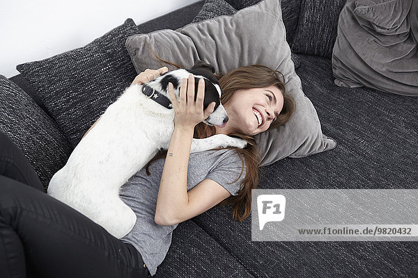 Young woman playing with dog on couch