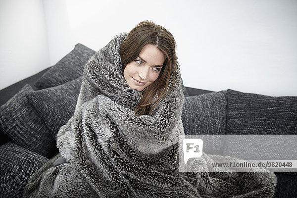 Young woman on couch wrapped in fur blanket