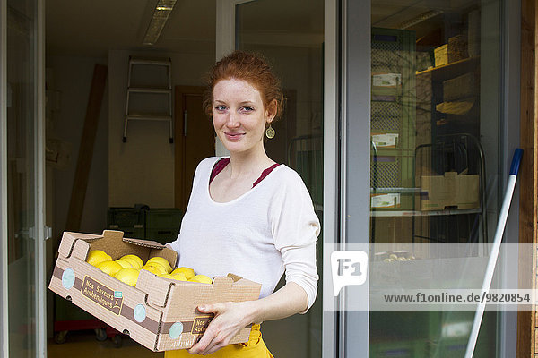 Porträt der lächelnden jungen Frau mit Zitronenschachtel vor dem Vollwertladen