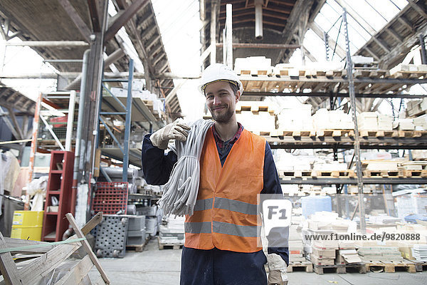 Smiling warehouseman in storehouse carrying tubes