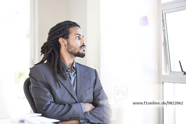 Businessman with dreadlocks looking through window in an office