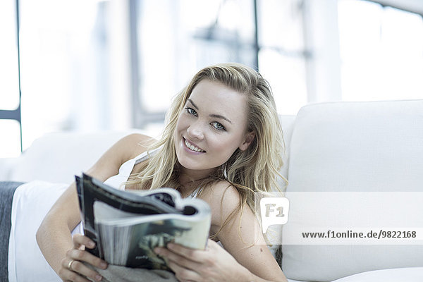 Porträt einer blonden Frau auf einer Couch mit Magazin