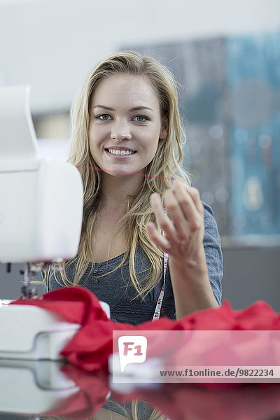 Porträt einer lächelnden jungen Frau bei der Arbeit mit einer Nähmaschine