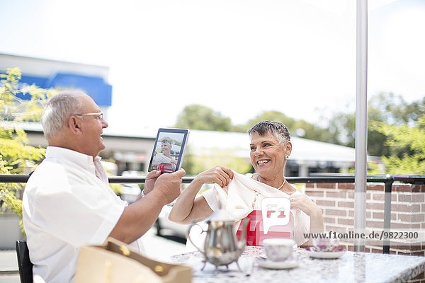 Älterer Mann fotografiert seine Frau mit einem Tablet-PC