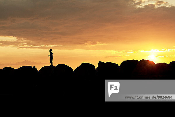 Silhouette of person standing on rocks at sunset