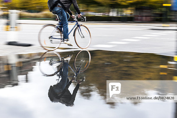 Person cycling along puddle