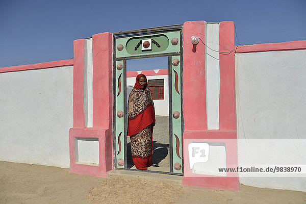 Nubian woman in typical bright dress  in front of her house  in the village of Umogaal in Dongola  Nile Valley  Nubia  Sudan  Africa