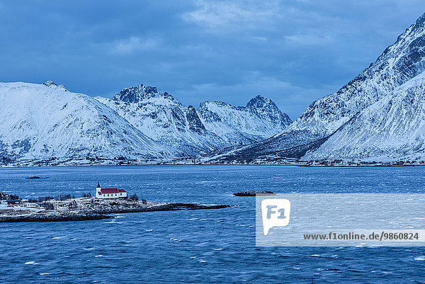 Small church with a red roof on a peninsula  snowy mountains behind  blue hour  Hamnoy island  Lofoten  Norway  Europe