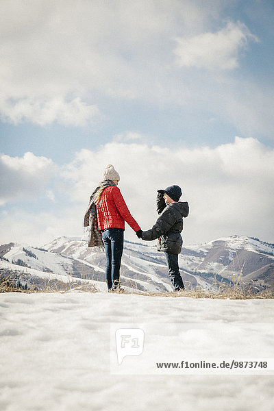A brother and sister holding hands and looking at the snowy landscape.
