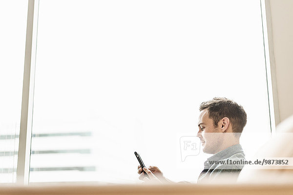 Ein Mann sitzt mit einem Smartphone in der Hand und hört seine Nachrichten ab.