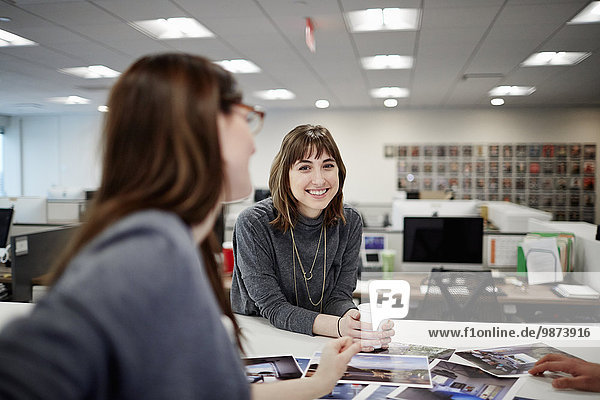 Zwei Frauen sitzen in einem Büro und unterhalten sich unterhaltend und lachend.