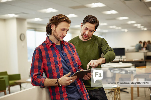 Zwei Männer schauen auf einen digitalen Tablet-Bildschirm in einem Büro.