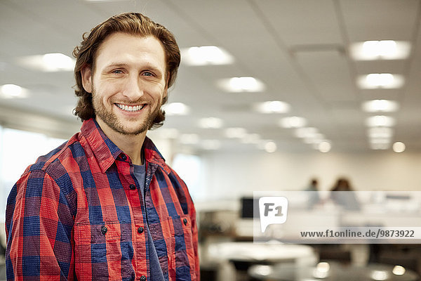 A handsome business man wearing a plaid shirt in a office.