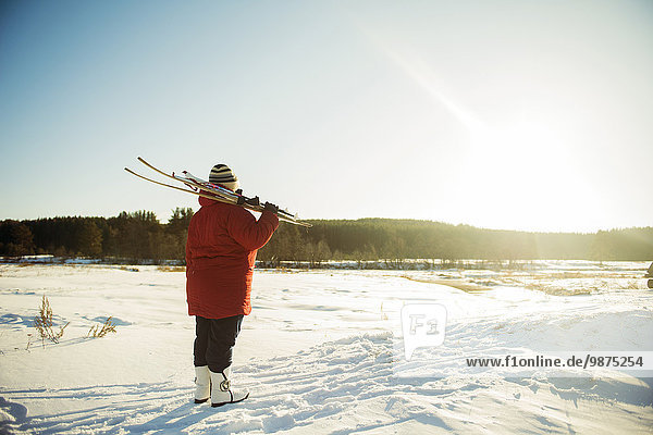 Caucasian woman carrying skis in snowy field
