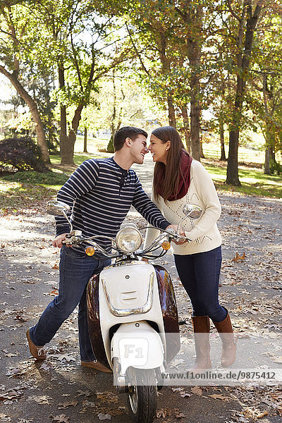 Couple kissing over scooter in suburban neighborhood