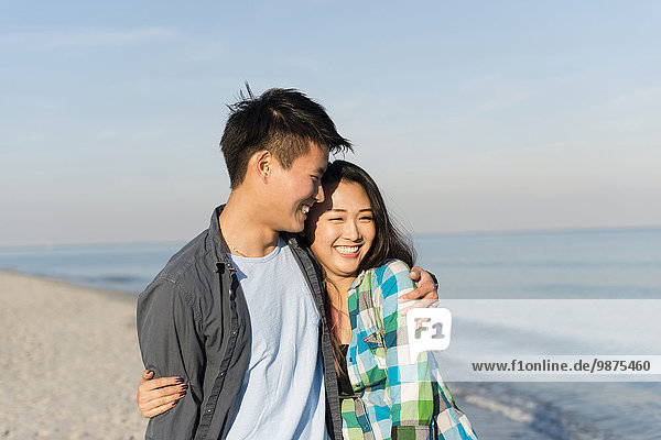 Smiling Korean couple hugging on beach