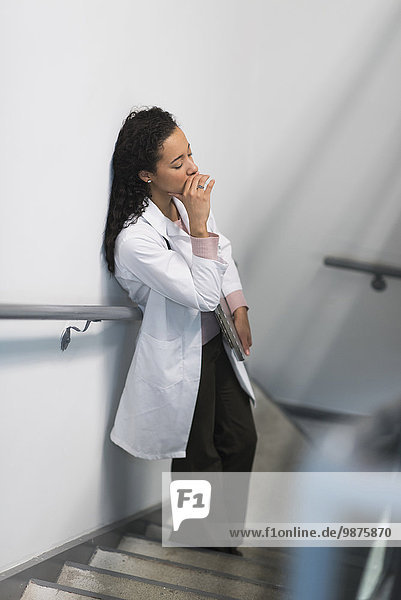 High angle view of stressed mixed race doctor standing on staircase