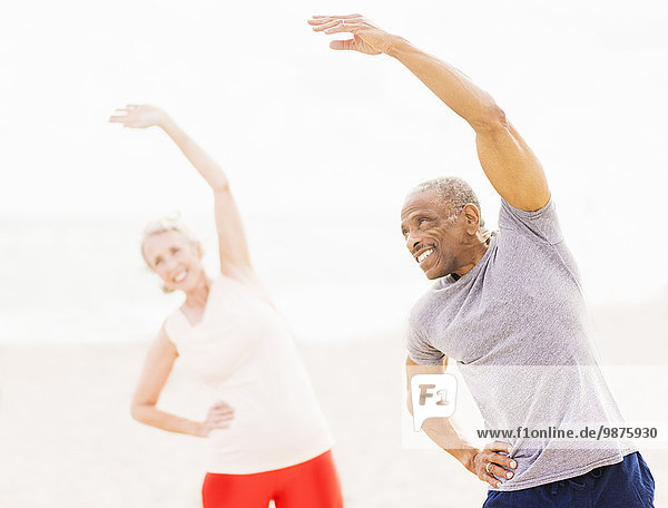 Older couple stretching together on beach