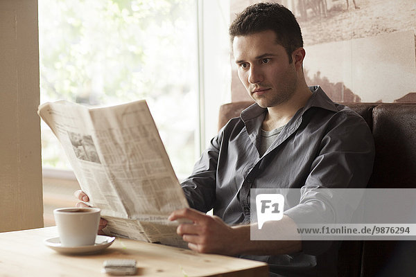 Man reading newspaper and drinking coffee in cafe