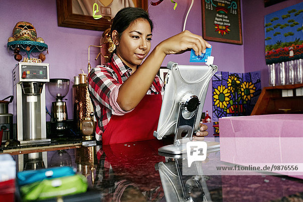 Hispanic barista using digital tablet register in coffee shop