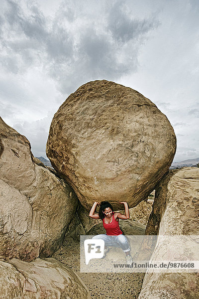 Hispanic woman lifting boulder on rocky hillside