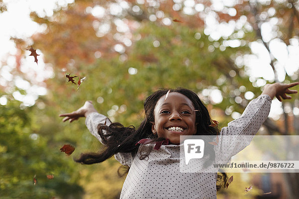 Low angle view of African American girl playing in autumn leaves