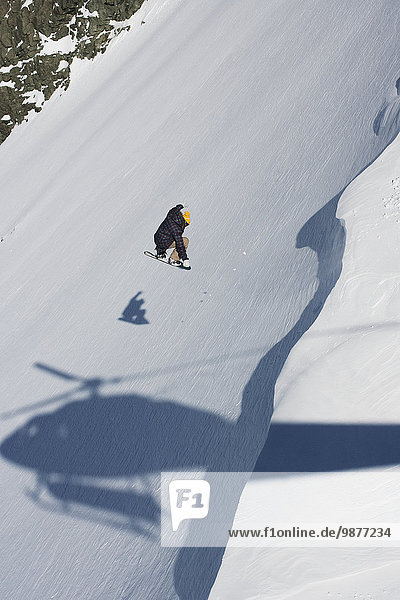Professional snowboarder  David Porcheron  makes a jump down a steep slope with the shadow of a helicopter looming  Methven  New Zealand