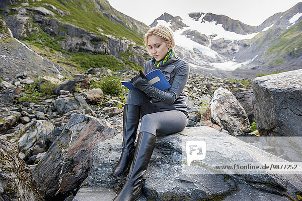 Woman sitting on a boulder and writing in her journal  Portage Valley  Southcentral Alaska
