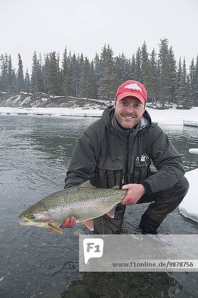 A Trout Fisherman Admires His Fat Rainbow Trout Before Releasing It Back Into The Kenai River On A Snowy Winter Day.