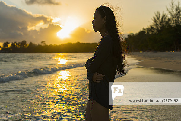 'A young woman stands posing on Sokha Beach at sunset; Sihanoukville  Cambodia'