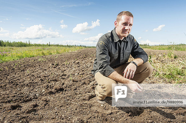Portrait of barley farmer kneeling over tilled field; Delta Junction  Alaska  United States of America