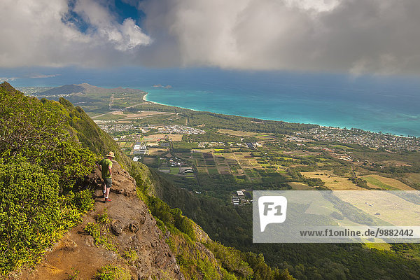 'A man standing on the edge of a cliff on the Kuliouou Ridge Trial enjoys the view of Oahu's windward side and the town of Waimanalo as the clouds roll in on a summer's day; Waimanalo  Oahu  Hawaii  United States of America'