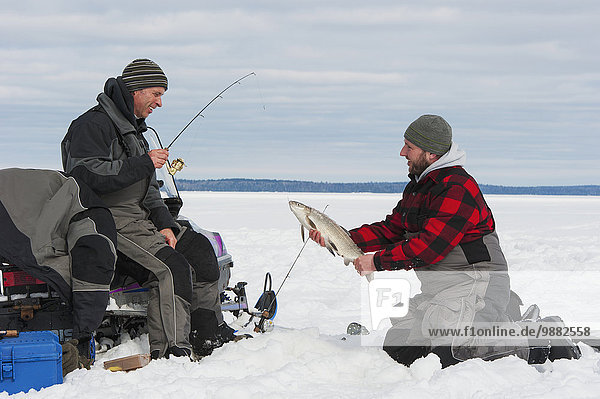 'Two ice fishermen  one holding a large whitefish; Ontario  Canada'