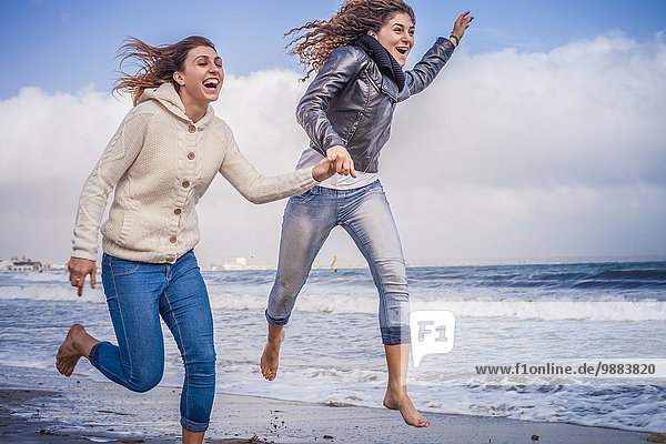 Zwei junge Frauen  die am Strand rennen und springen.