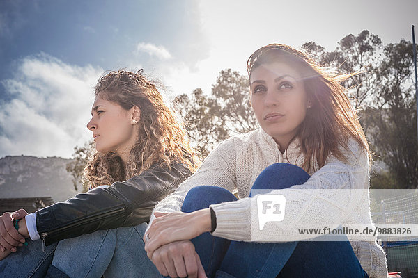 Zwei mürrische junge Frauen  die am luftigen Strand sitzen.