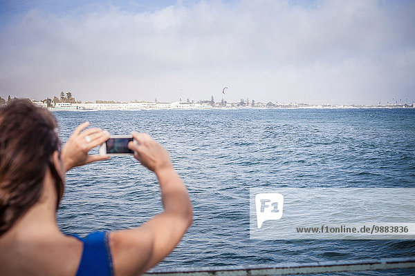 Junge Frau fotografiert Meerblick auf dem Smartphone