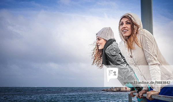 Zwei junge Frauen  die vom Pier aus auf das Meer schauen.