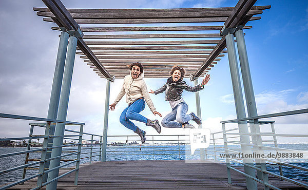 Zwei junge Freundinnen springen unisono auf der Seebrücke.