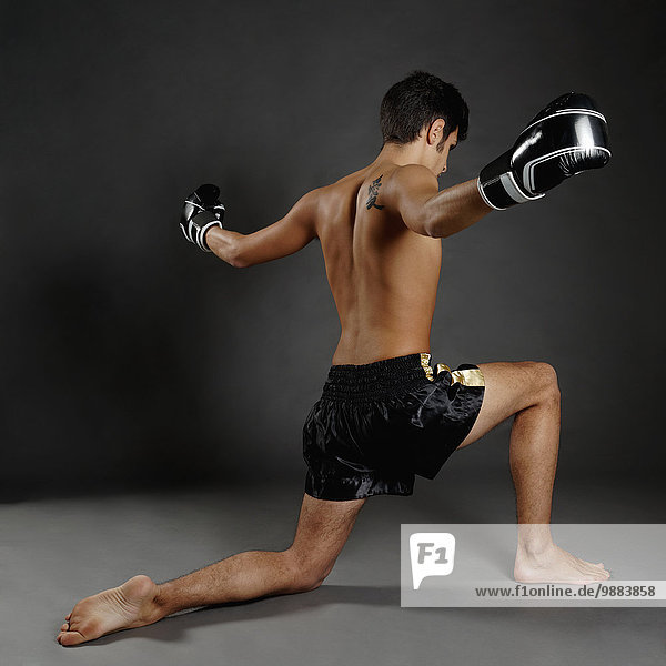 Rückansicht eines jungen Mannes mit Boxhandschuhen auf einem Knie
