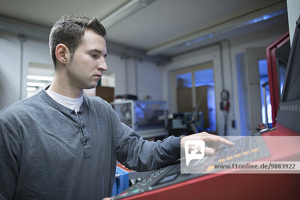 Young male technician using control panel for machine in workshop