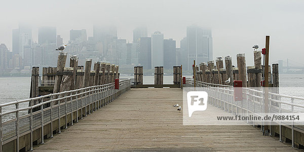 View of the skyline through the fog from a wooden pier; New York City  New York  United States of America