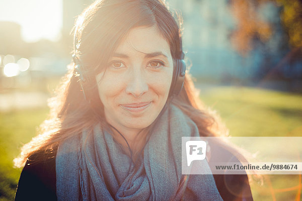 Porträt einer erwachsenen Frau  die im Park Kopfhörer hört.