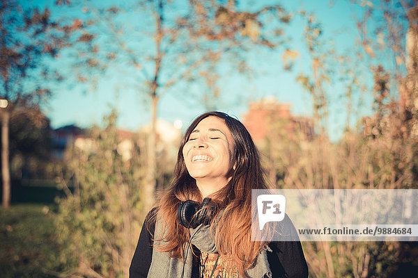 Mid adult woman laughing with eyes closed in park