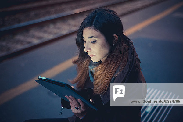 Mittlere erwachsene Frau mit digitalem Tablett auf dem Bahnsteig in der Abenddämmerung