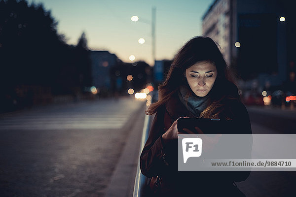 Mittlere erwachsene Frau mit digitalem Tablett auf der Straße in der Abenddämmerung